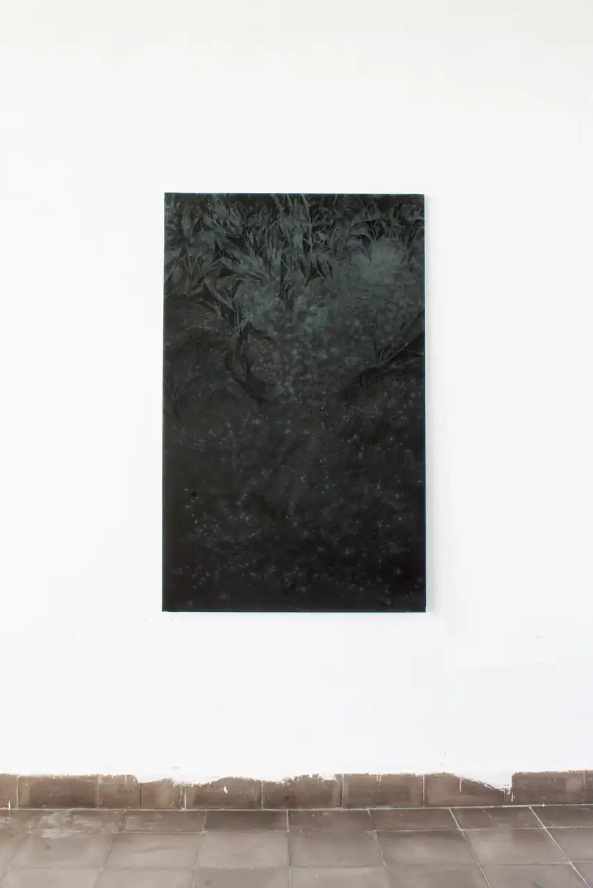 Pintura vertical oscura de María Vera colgada en una pared blanca sobre un zócalo de baldosas; en su parte superior se distinguen formas vegetales claras.