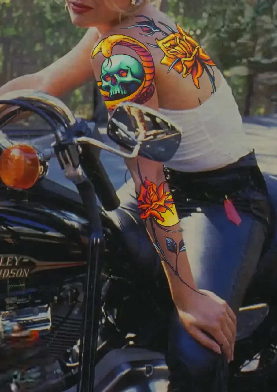 Diseño de María Vera mostrado en mockup sobre una fotografía de archivo: mujer rubia sobre una moto, con una calavera verde enroscada por una serpiente y flores naranjas en el hombro y una rosa en el antebrazo.