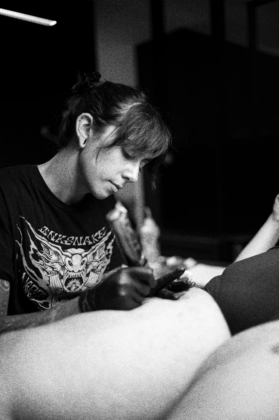 María tatuando una pierna en el estudio, en blanco y negro.