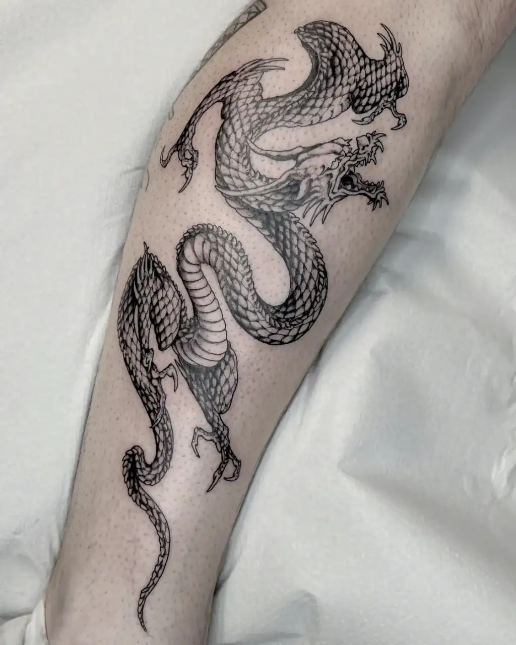 Tatuaje en la pierna: dragón oriental de trazo fino.